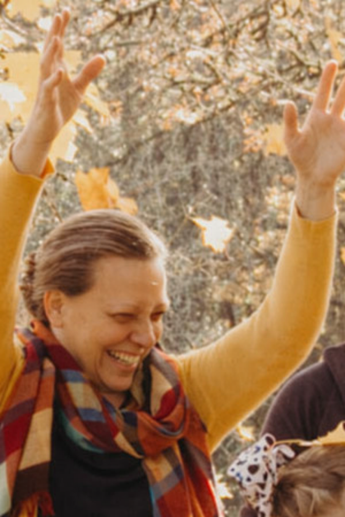 Fall family photo shoot - Julie with hands above her head from having tossed fall leaves into the air above her.
